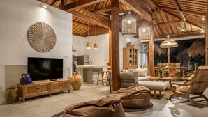 Amplia sala de estar con televisor, muebles de madera y comedor con techo de paja.