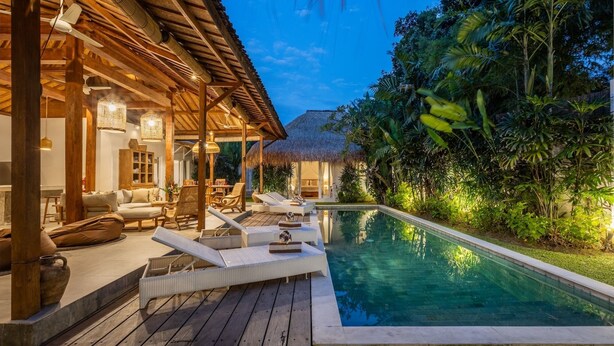 Un área junto a la piscina con sillones reclinables, una terraza de madera y una estructura de techo de paja.
