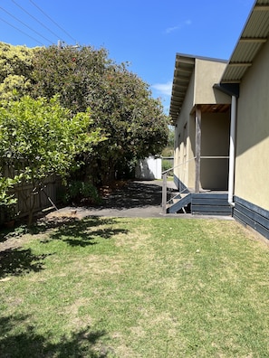 A residential backyard with a wooden fence, a tree, and a staircase leading to a building. - Barwon Bliss Beach House (Barwon Heads)