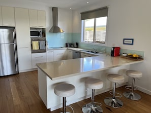 A modern kitchen with a central island, stainless steel appliances, and a window with a view. - Barwon Bliss Beach House (Barwon Heads)