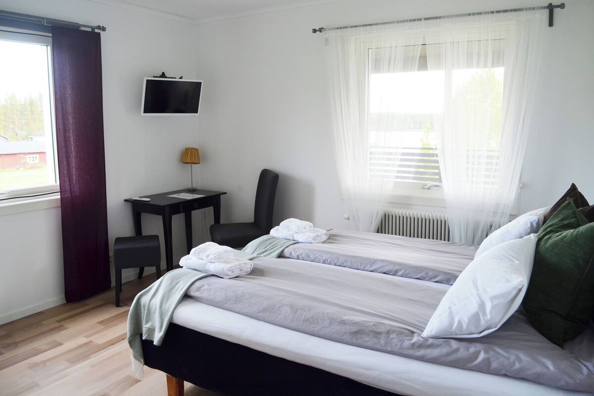 A hotel room with two beds, a desk, a chair, a TV, and a window with curtains.