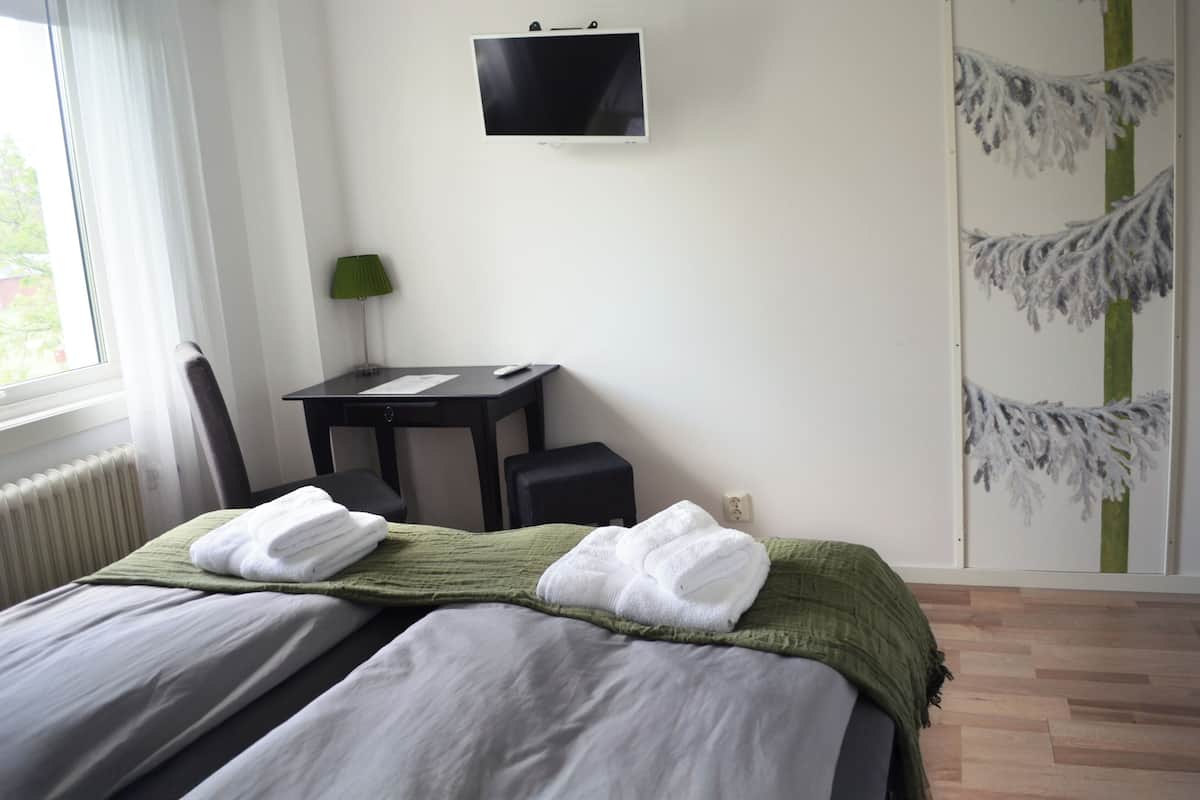 A hotel room with a bed, a desk, a chair, a TV, and a window.