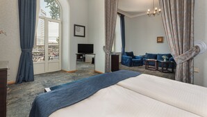 A hotel room with a large bed, a seating area with a sofa and armchairs, a television, and a view of the city through a large window. - Hotel Bella Casa (Tbilisi)