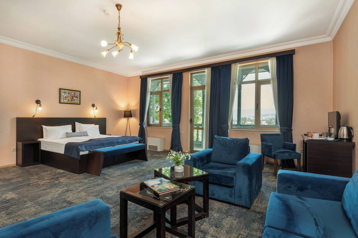 A hotel room with a bed, two blue sofas, a coffee table, and a desk with a kettle.