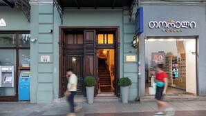 A building with a wooden entrance, a blue ATM, and a storefront with a sign. - Hotel Bella Casa (Tbilisi)