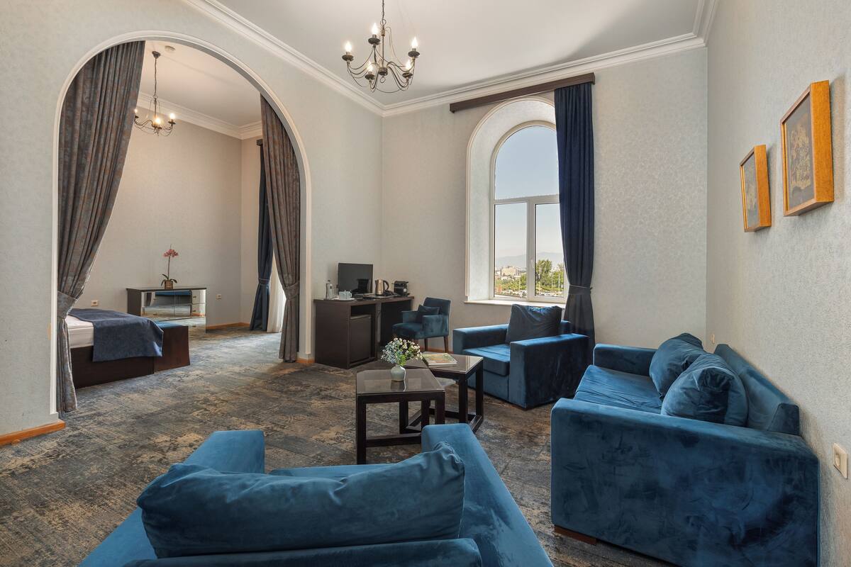 A room with a large window, a desk, a sofa, and a bed.