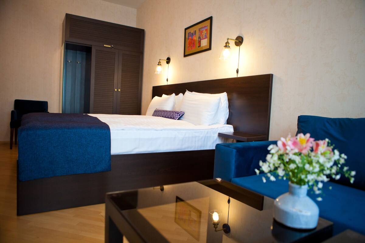 A hotel room with a bed, a sofa, a coffee table, and a vase with flowers.