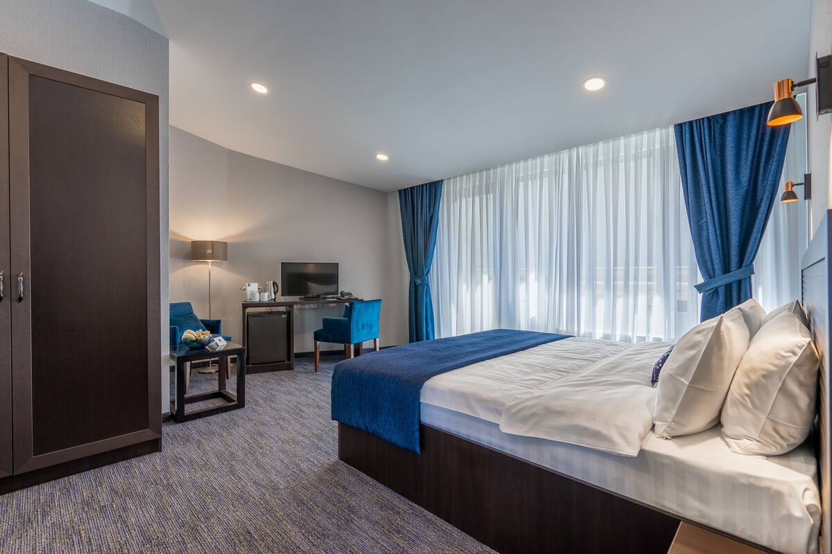 A hotel room with a bed, desk, chair, and wardrobe.