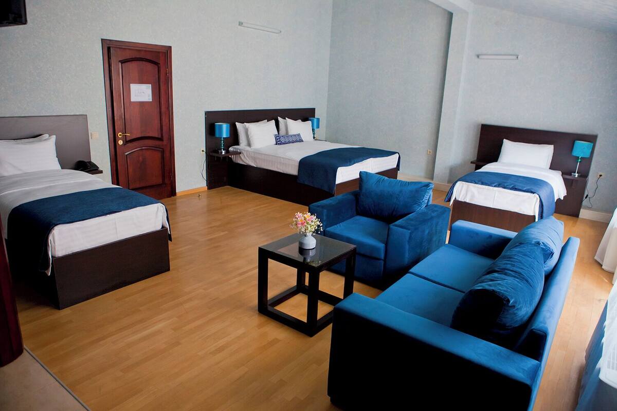 A hotel room with two single beds, a sofa, a small table with a vase, and a wooden floor.