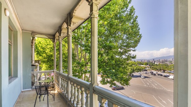 A balcony with a table and chairs, overlooking a parking lot and cityscape. - Hotel Bella Casa (Tbilisi)