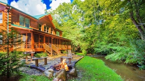 A log cabin with a deck and a fire pit in a lush, green forest setting. - Creekside Getaway: Top Amenities, Game Room, Fire Pit area on the creek, Ample Parking, Gatlinburg! (Pigeon Forge)