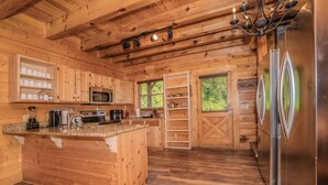 A wooden cabin kitchen with a central island, stainless steel appliances, and built-in shelves. - Creekside Getaway: Top Amenities, Game Room, Fire Pit area on the creek, Ample Parking, Gatlinburg! (Pigeon Forge)