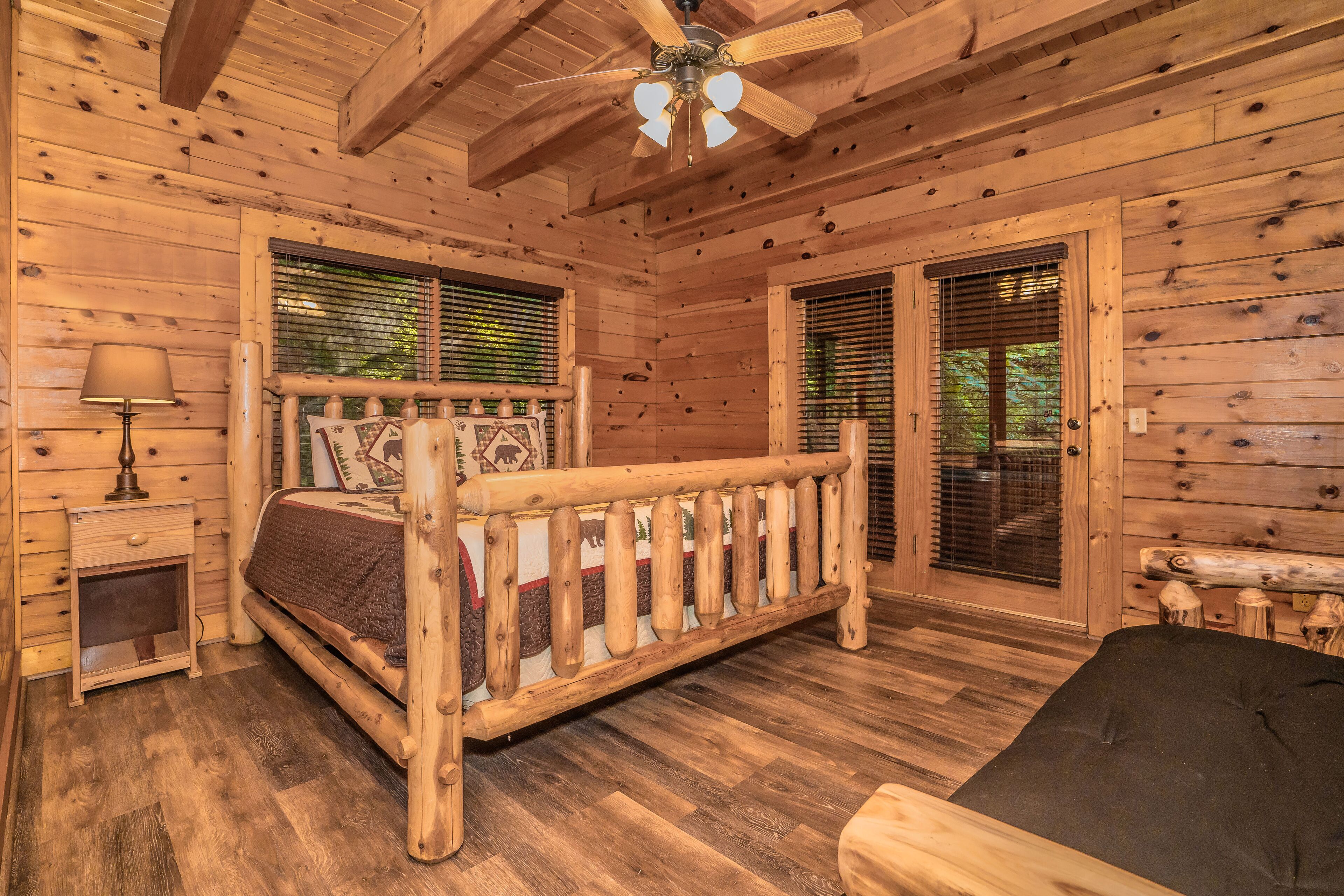 A wooden cabin bedroom with a bed, a nightstand, a lamp, and a ceiling fan.