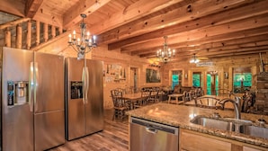 A spacious kitchen with stainless steel appliances, a granite countertop, and a dining area with wooden chairs and a chandelier. - Creekside Getaway: Top Amenities, Game Room, Fire Pit area on the creek, Ample Parking, Gatlinburg! (Pigeon Forge)