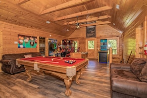 A wooden interior with a pool table, leather sofas, and various recreational equipment. - Creekside Getaway: Top Amenities, Game Room, Fire Pit area on the creek, Ample Parking, Gatlinburg! (Pigeon Forge)