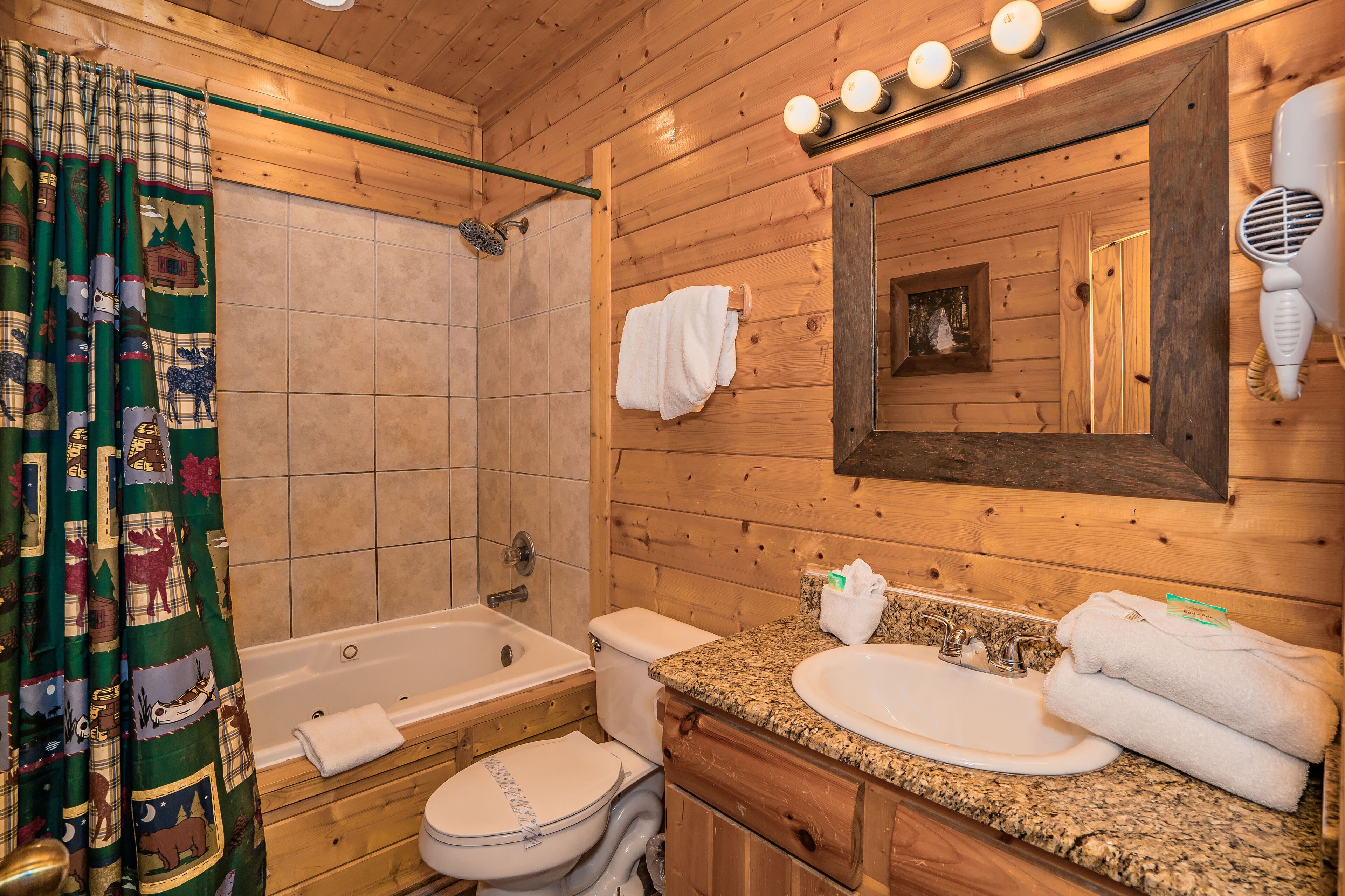 Baño de cabaña de madera con bañera, inodoro, lavamanos y un espejo con iluminación.