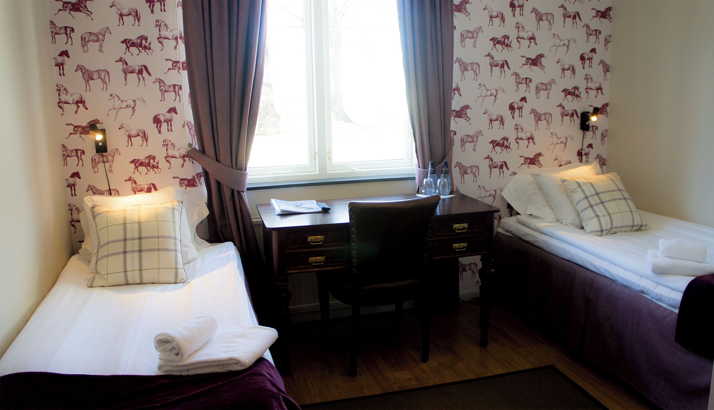 A hotel room with two single beds, a desk, and a chair.