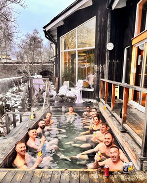 A hot tub area with wooden decking, a stone bridge, and a large window overlooking a snowy landscape. - Färna Herrgård & Spa (Kolsva)