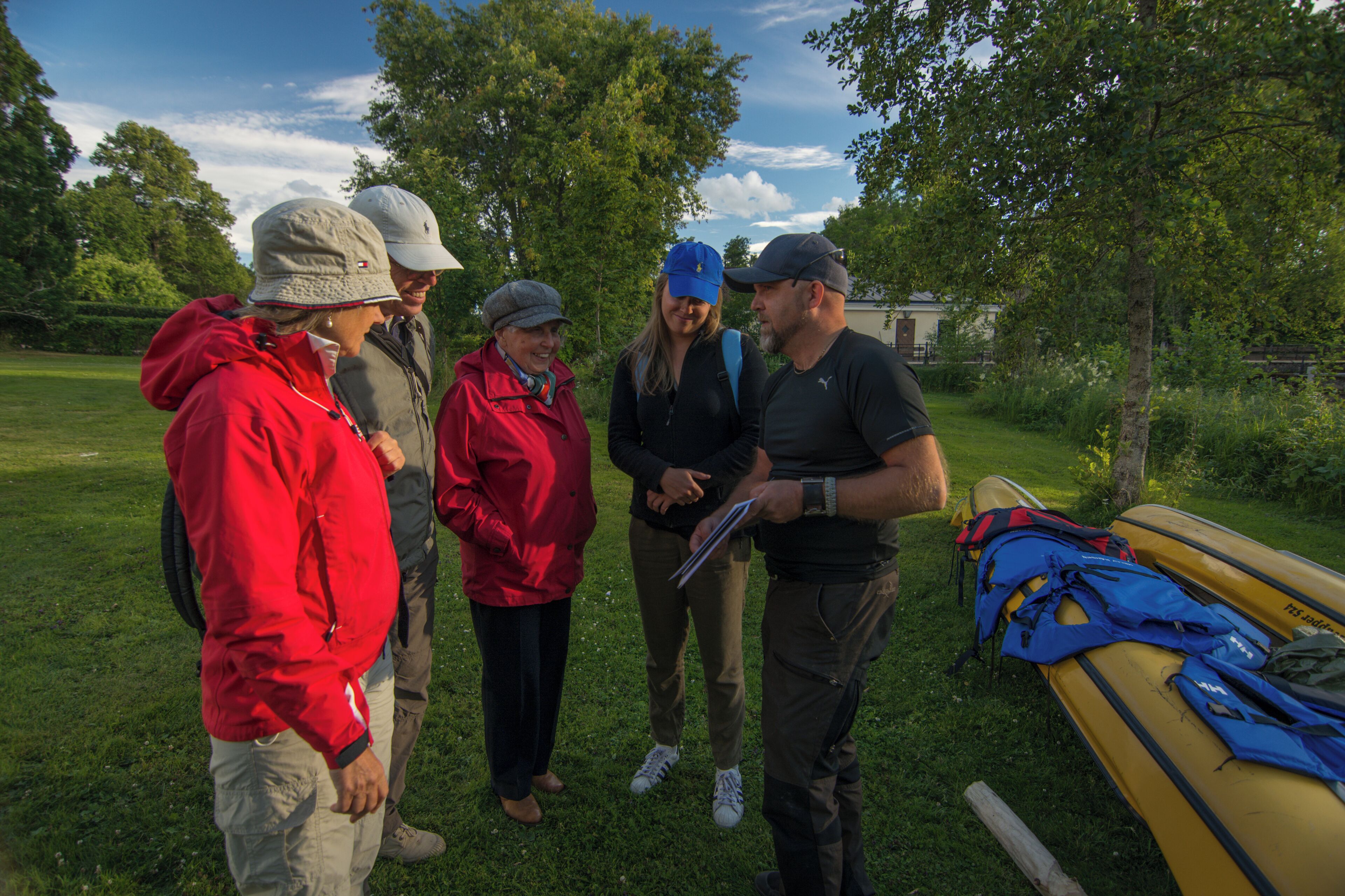 A group of people standing outdoors near a yellow kayak, discussing something.