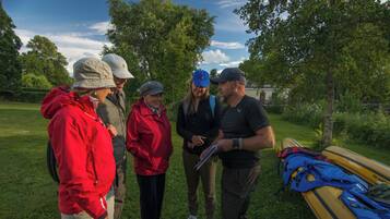 A group of people standing outdoors near a yellow kayak, discussing something.