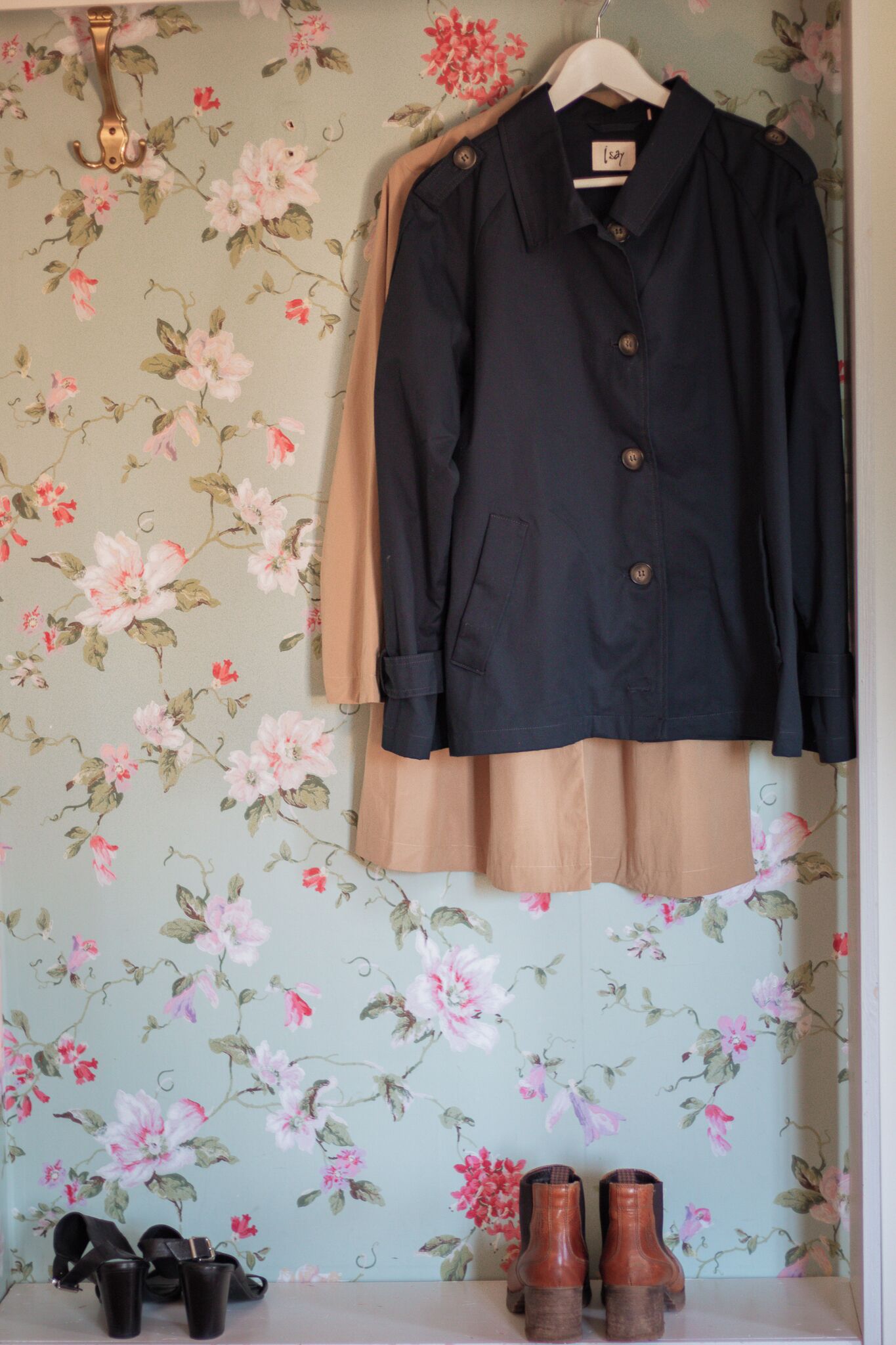 A room with floral wallpaper, a black coat on a hanger, and a pair of shoes on the floor.