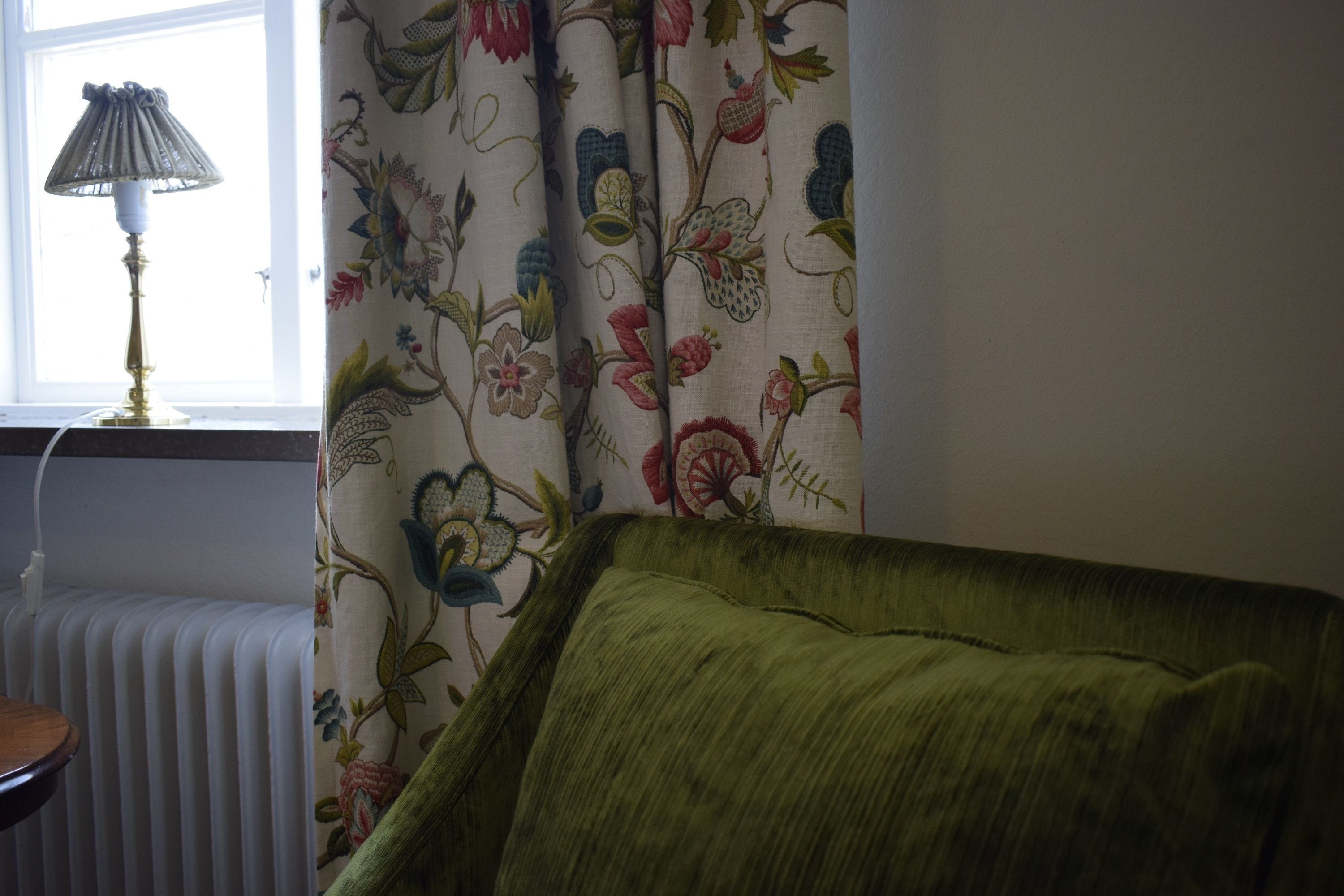 Et værelse med en radiator, en lampe og en grøn sofa.