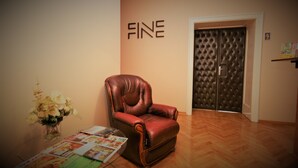 Quarto com poltrona de couro, mesa de vidro com revistas, vaso com flores e porta com a placa 'FINE'.