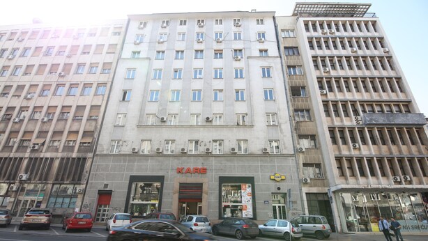 Um edifício de vários andares com uma placa grande da 'KARE', vários carros estacionados e um céu claro.