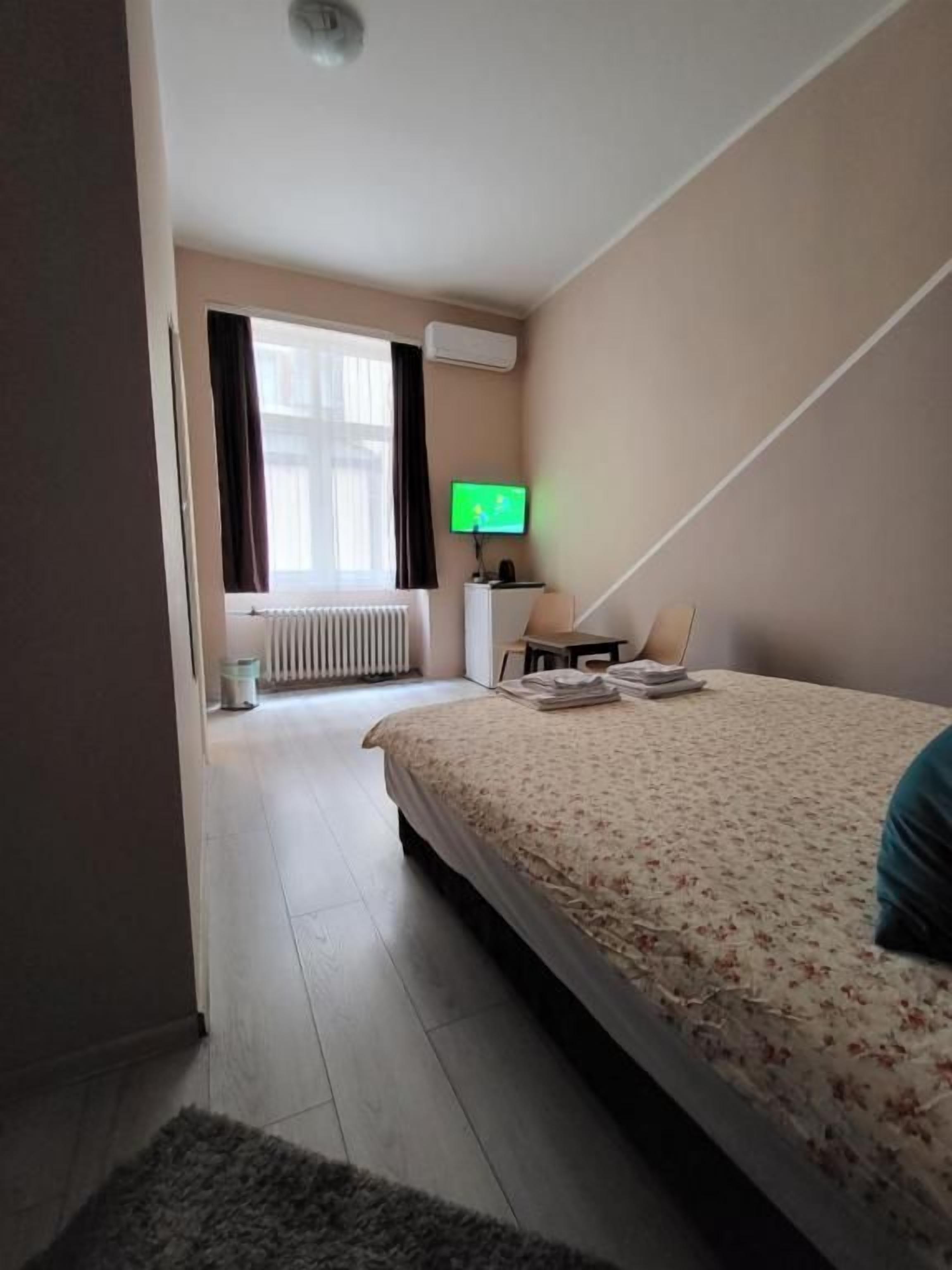 Une chambre d’hôtel avec un lit, une télévision, un radiateur et une fenêtre avec des rideaux.