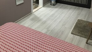 Quarto com cama, janela com cortinas leves, radiador e porta para um banheiro.