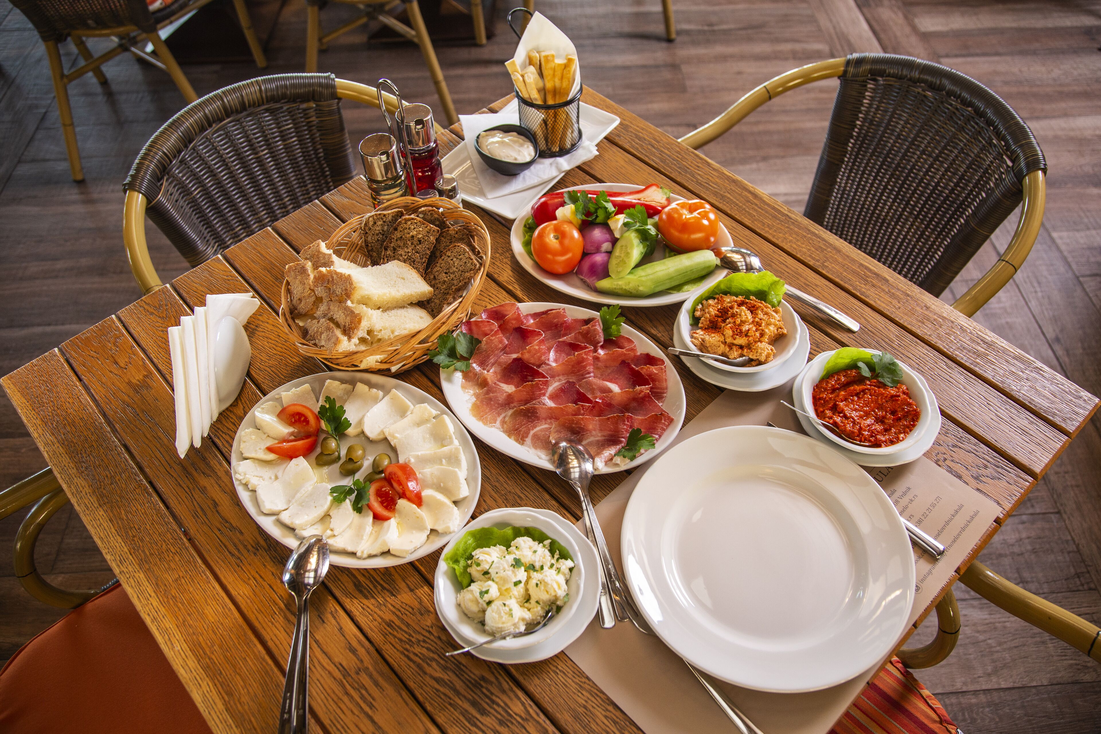 Un tavolo da pranzo in legno con diversi piatti, tra cui pane, formaggio, pomodori e olive.