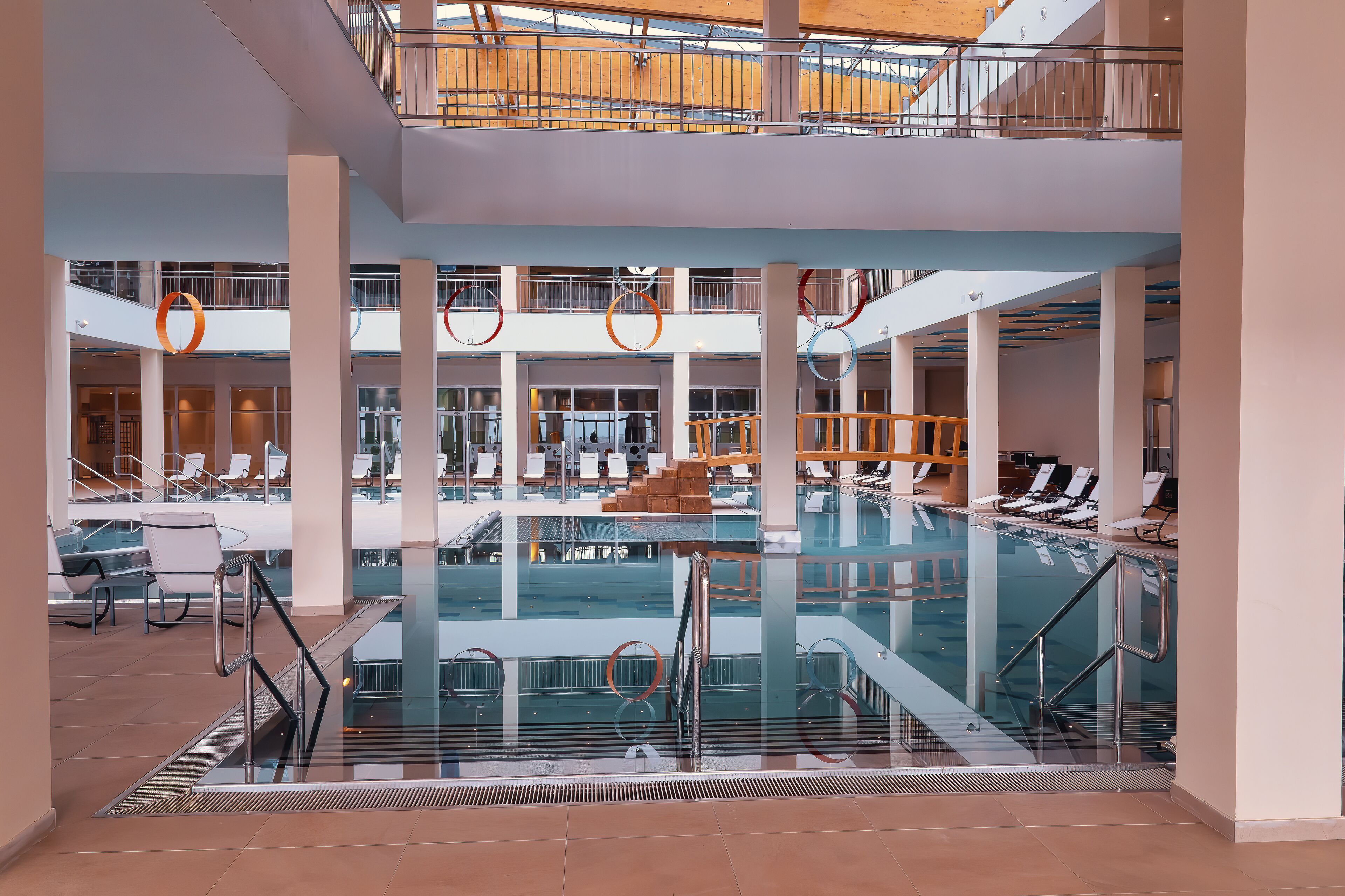 Une vaste piscine intérieure à plusieurs niveaux, dotée de cloisons en verre transparent et d’un escalier central.