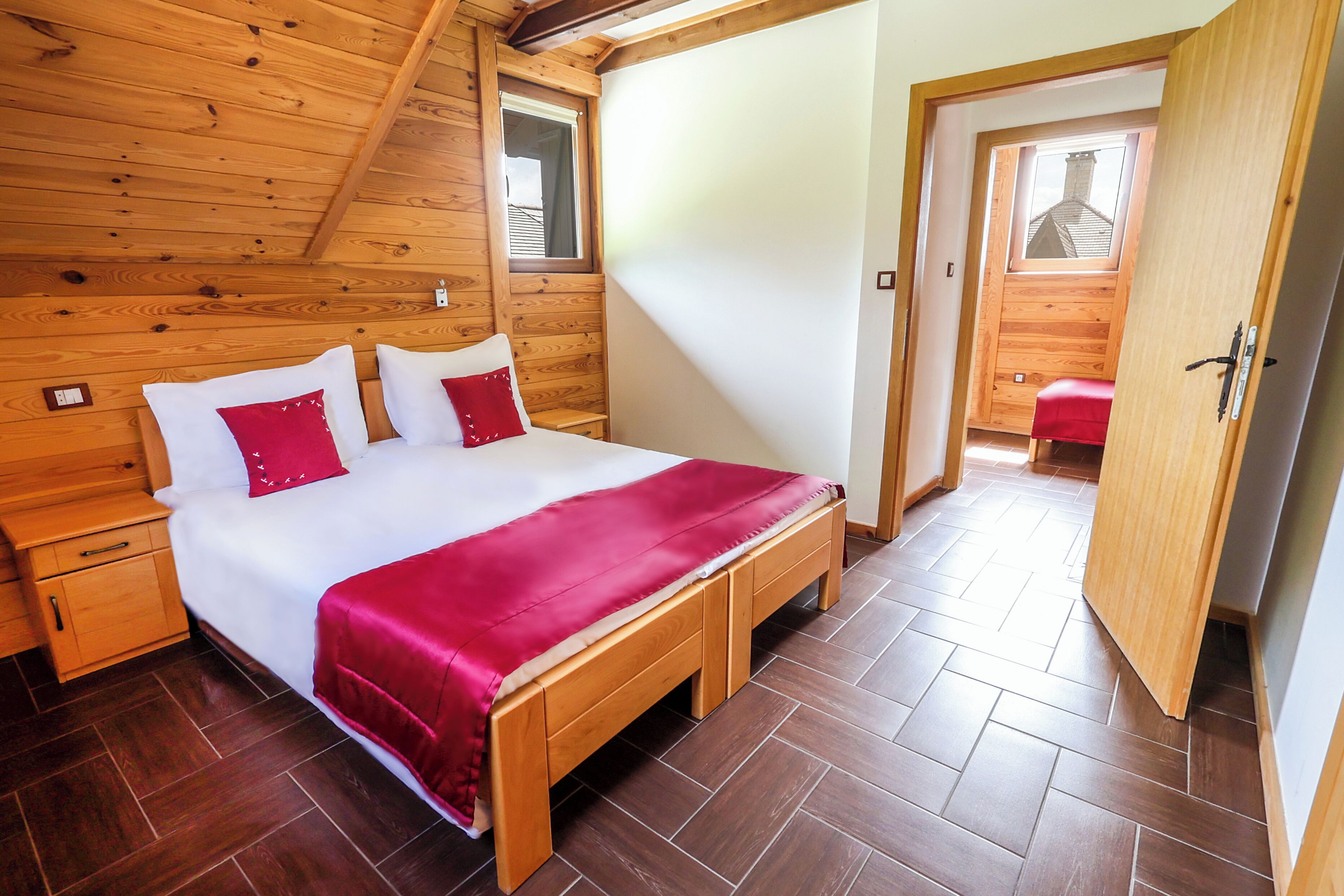 A wooden-paneled bedroom with a bed, a bench, and a door leading to another room.