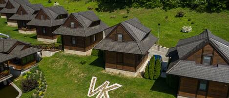 A cluster of wooden cabins with sloped roofs, arranged in a row on a grassy hillside.