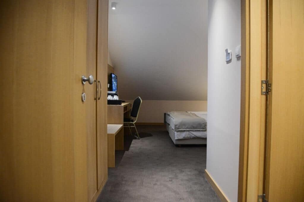 Un pasillo estrecho que conduce a un dormitorio con escritorio y silla, cama y una ventana pequeña.