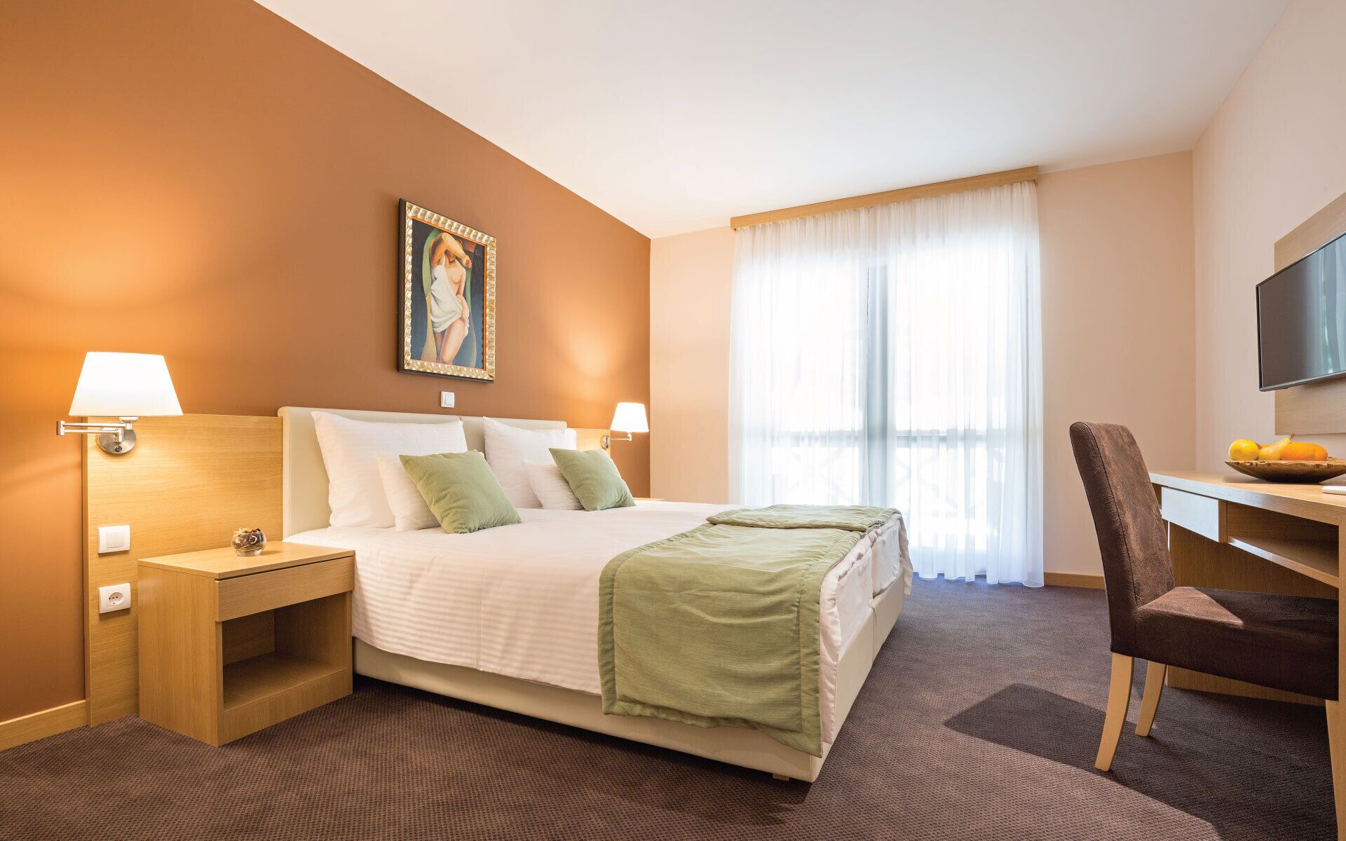 Una habitación de hotel con cama, lámparas de noche, un escritorio con silla, televisión y ventana con cortinas.