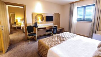 A hotel room with a bed, a desk with a computer, a chair, a TV, and a window with curtains.