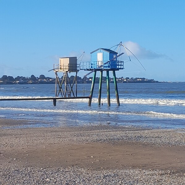 Une plage avec deux structures surélevées, l’une de couleur beige et l’autre bleue, reliées par une échelle.