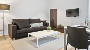 A modern living room with a sofa, coffee table, TV, and a desk with chair. - One Bedroom Apartment with balcony (Barcelona)