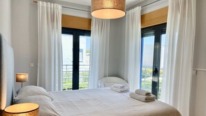 A hotel room with a large bed, two bedside lamps, a view of greenery through the windows, and a balcony. - Villa Palmela in Serra da Arrábida (Palmela)