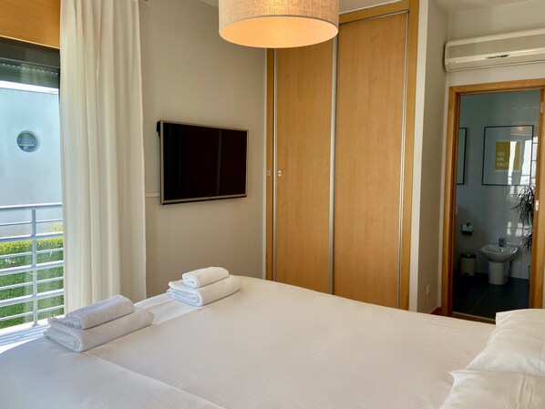 A hotel room with a bed, a TV, a wardrobe, and a bathroom visible through an open door. - Villa Palmela in Serra da Arrábida (Palmela)