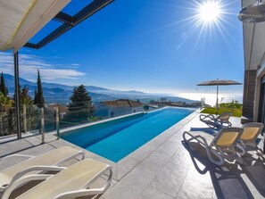Un área de piscina exterior moderna con agua azul cristalina, sol y vistas a montañas.