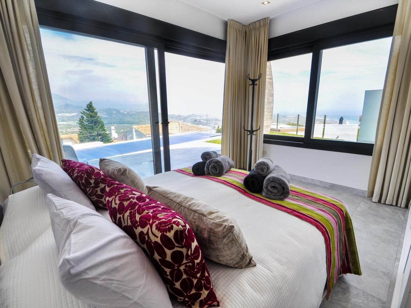 Een moderne slaapkamer met een groot bed, meerdere kussens, een gestreept dekbed en handdoeken.