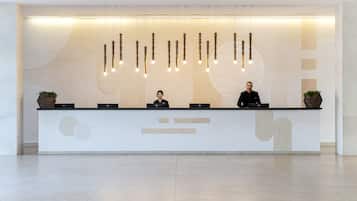 Un mostrador de recepción con dos empleados, diseño moderno con lámparas colgantes y decoración minimalista en la pared.