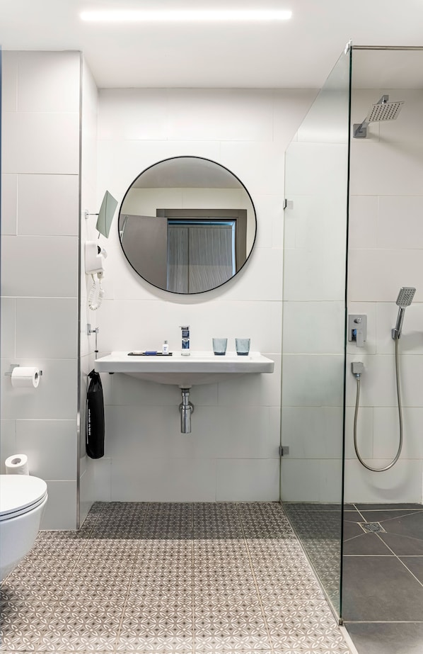 Une salle de bain moderne avec un miroir rond, un lavabo blanc et une cabine de douche en verre.