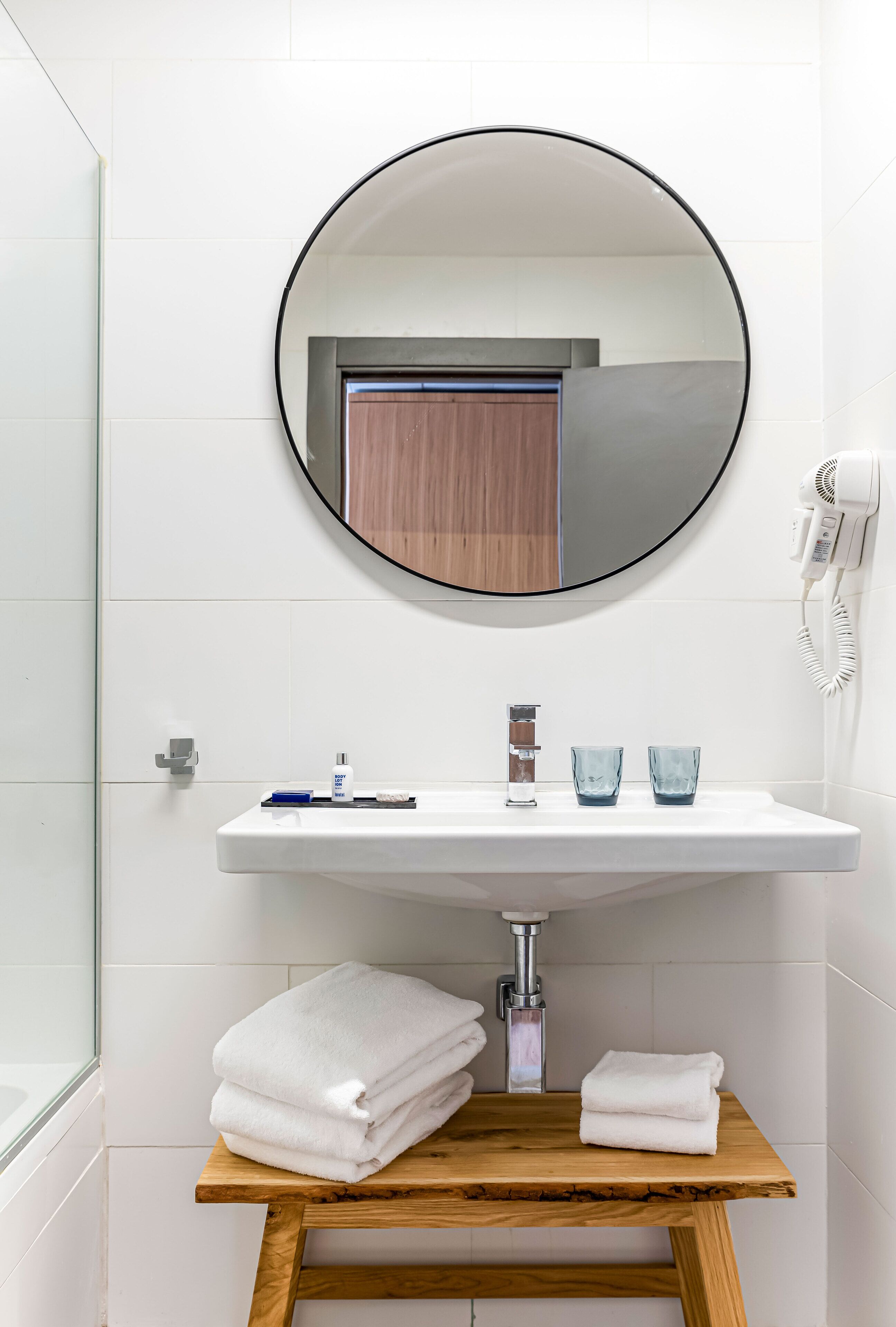 A bathroom with a round mirror, white sink, and wooden vanity.