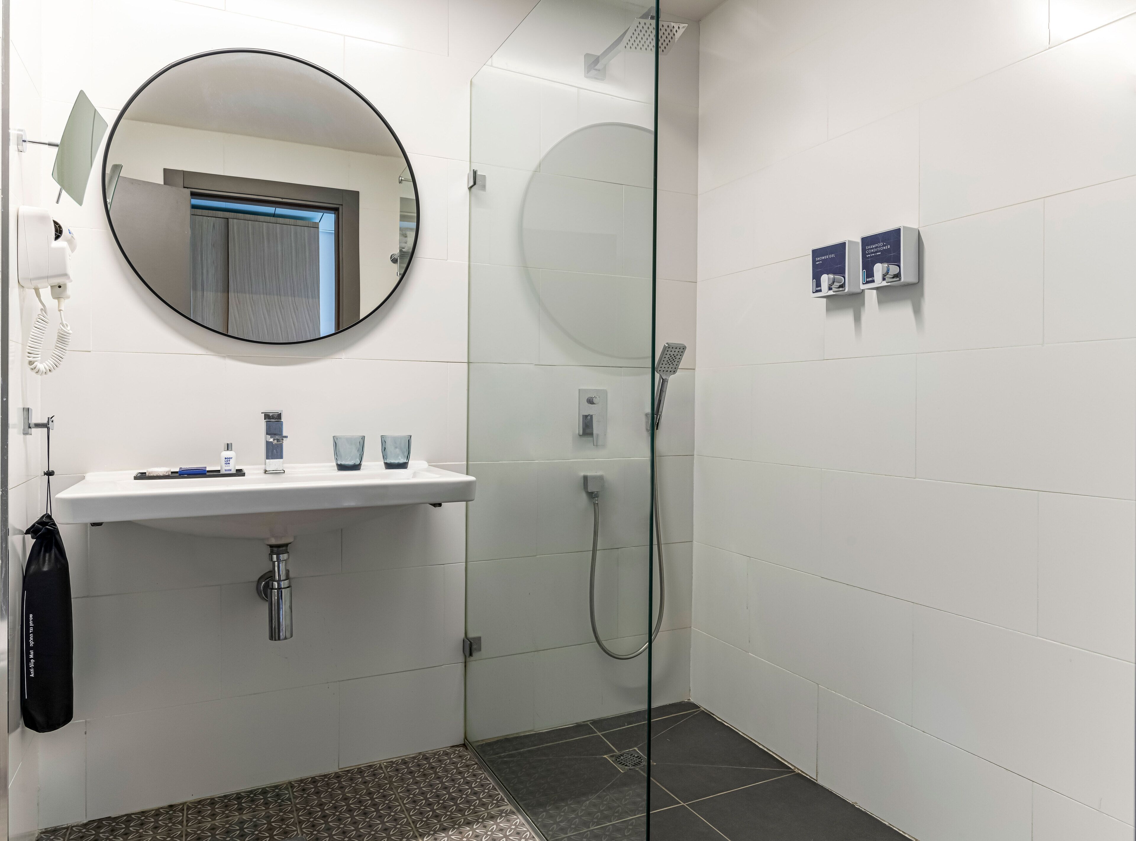 A modern bathroom with a glass-enclosed shower, a white sink with two glasses, and a mirror.