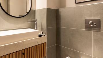 Un baño moderno con un lavamanos rectangular, un espejo redondo, un inodoro y un perchero para toallas.