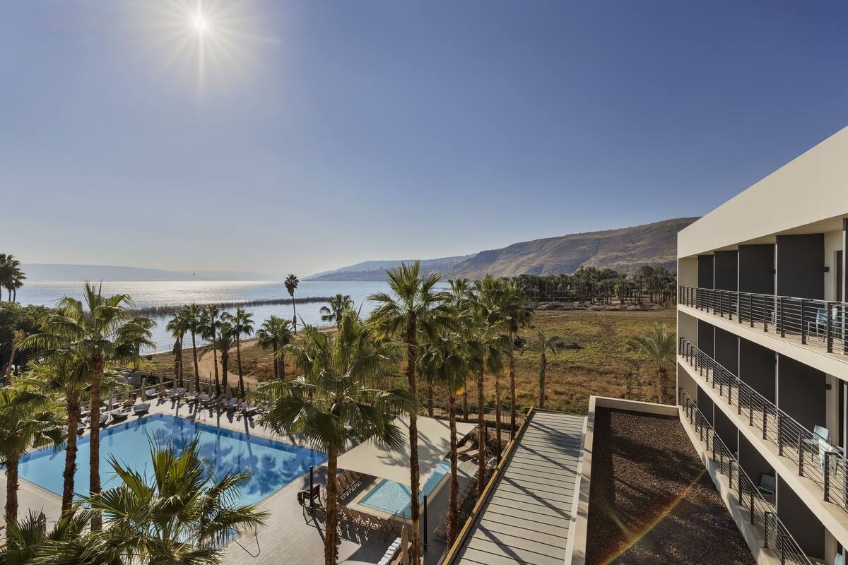 Un espace piscine agrémenté de palmiers, avec vue sur l’océan, et un bâtiment doté de balcons.