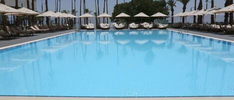 A swimming pool with lounge chairs and umbrellas, surrounded by palm trees.
